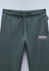 Grüne Baumwollmischung-Jogginghosen mit elastischem Bund, Seitentaschen und einem kontrastierenden Logopatch mit Text und Flaggen auf dem Oberschenkel.