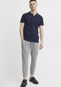 Marineblå polo med krave og tre knapper, parret med lysegrå tapered bukser med sidelister og sorte slip-on sko.