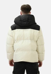 Giacca a vento con cappuccio in crema e nero, caratterizzata da sezioni imbottite, un cappuccio completo e una vestibilità rilassata. Tessuto liscio con una texture morbida.