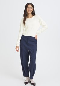 Top en tricot crème à manches longues avec un col rond, associé à un pantalon taille haute bleu marine avec poches avant et fermeture à bouton.