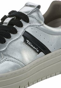 Baskets en argent métallique avec des lacets noirs, présentant une texture lisse, une bande latérale noire contrastante et une semelle blanche texturée.