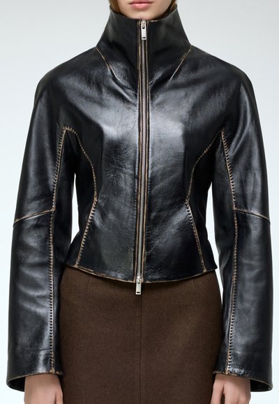 Chaqueta de cuero negra con cuello alto, cremallera frontal y costuras en contraste. Presenta un diseño ajustado y hombros estructurados.