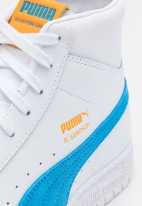 Baskets blanches Puma R. Sampson avec bande en daim bleu et marquage orange sur la languette et le côté.