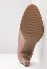 Chaussure à talon haut en cuir rose avec une semelle texturée, présentant un design incurvé et un bout arrondi. Le talon est de forme basse et carrée.