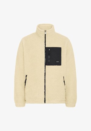 Jachetă din fleece crem cu guler înalt, având un buzunar pe piept cu fermoar negru și accente negre de-a lungul fermoarului și pe laterale.