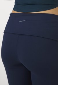 Gros plan d'une personne portant des leggings Nike bleu foncé avec une taille haute et un top court laissant apparaître le ventre.