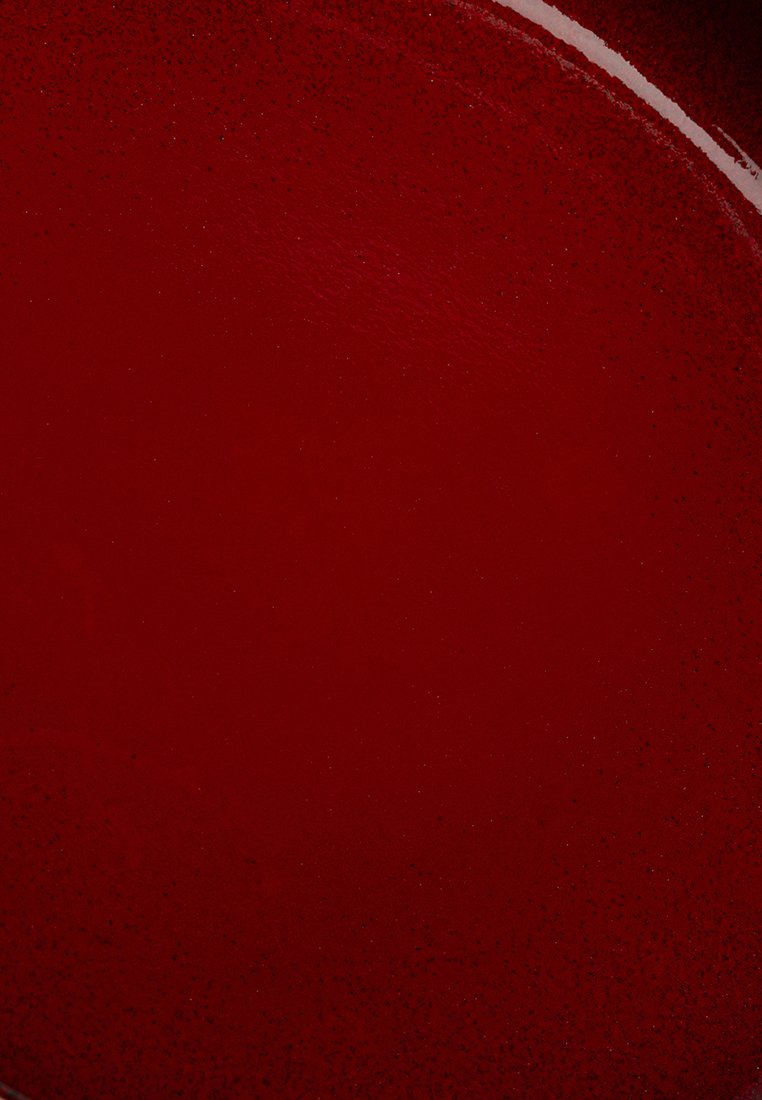 Runde rote Platte mit glatter Oberfläche, die feine Sprenkel für Textur aufweist. Der Rand ist leicht unregelmäßig und verleiht ein handgefertigtes Aussehen.