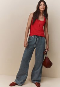 Rode, textuurvolle tanktop met knopen, gecombineerd met losse lichtblauwe denim broek. Accessoires zijn een rode tas en geweven rode schoenen.