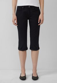 Czarne dżinsowe spodnie capri z podwiniętymi mankietami, pięcioma kieszeniami i gładką teksturą. Połączone z czarnymi balerinami z ćwiekami.