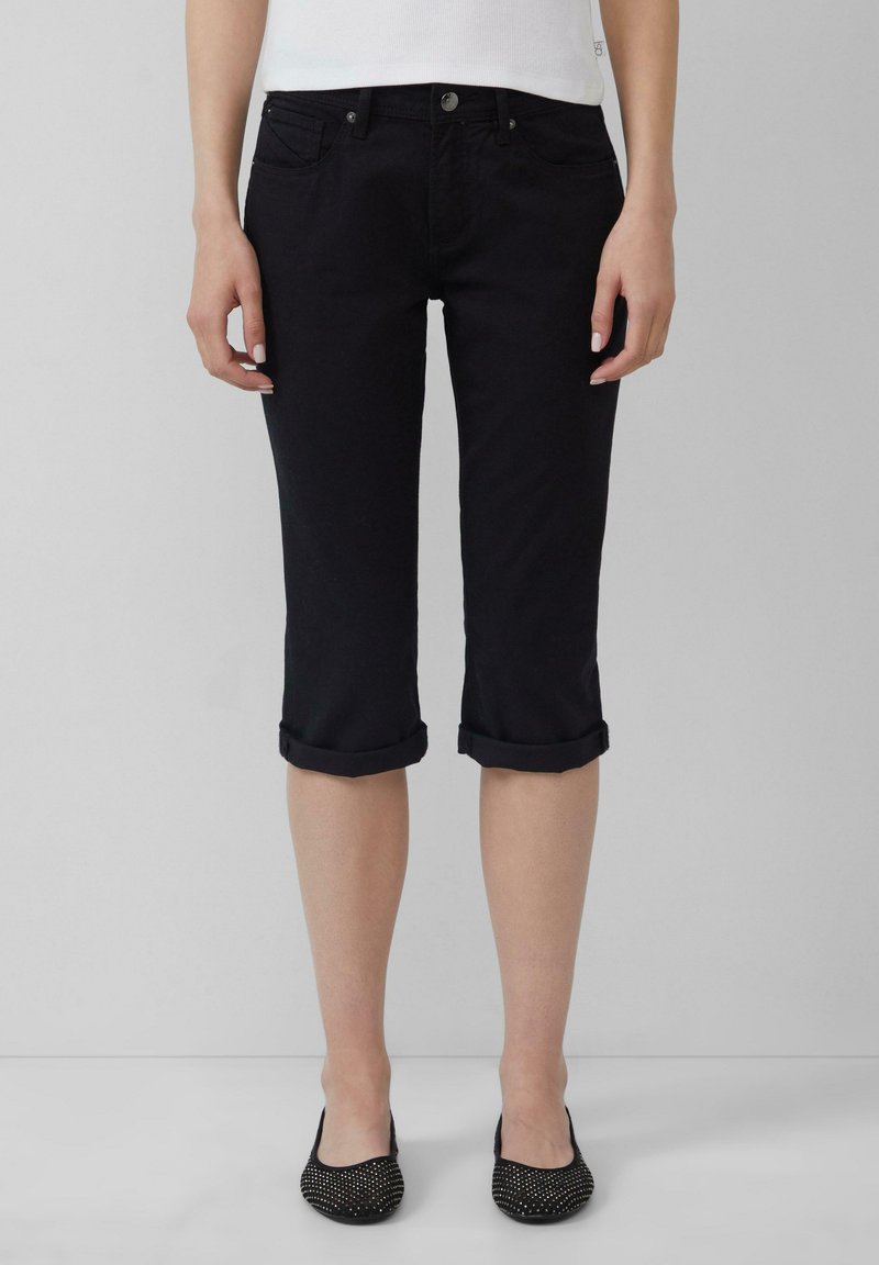 Czarne dżinsowe spodnie capri z podwiniętymi mankietami, pięcioma kieszeniami i gładką teksturą. Połączone z czarnymi balerinami z ćwiekami.