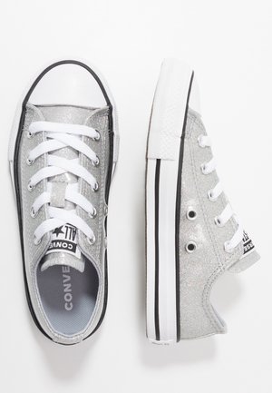 Baskets basses Converse pailletées argentées avec lacets blancs et semelles blanches à rayures noires, une chaussure vue de face, l’autre vue de côté.