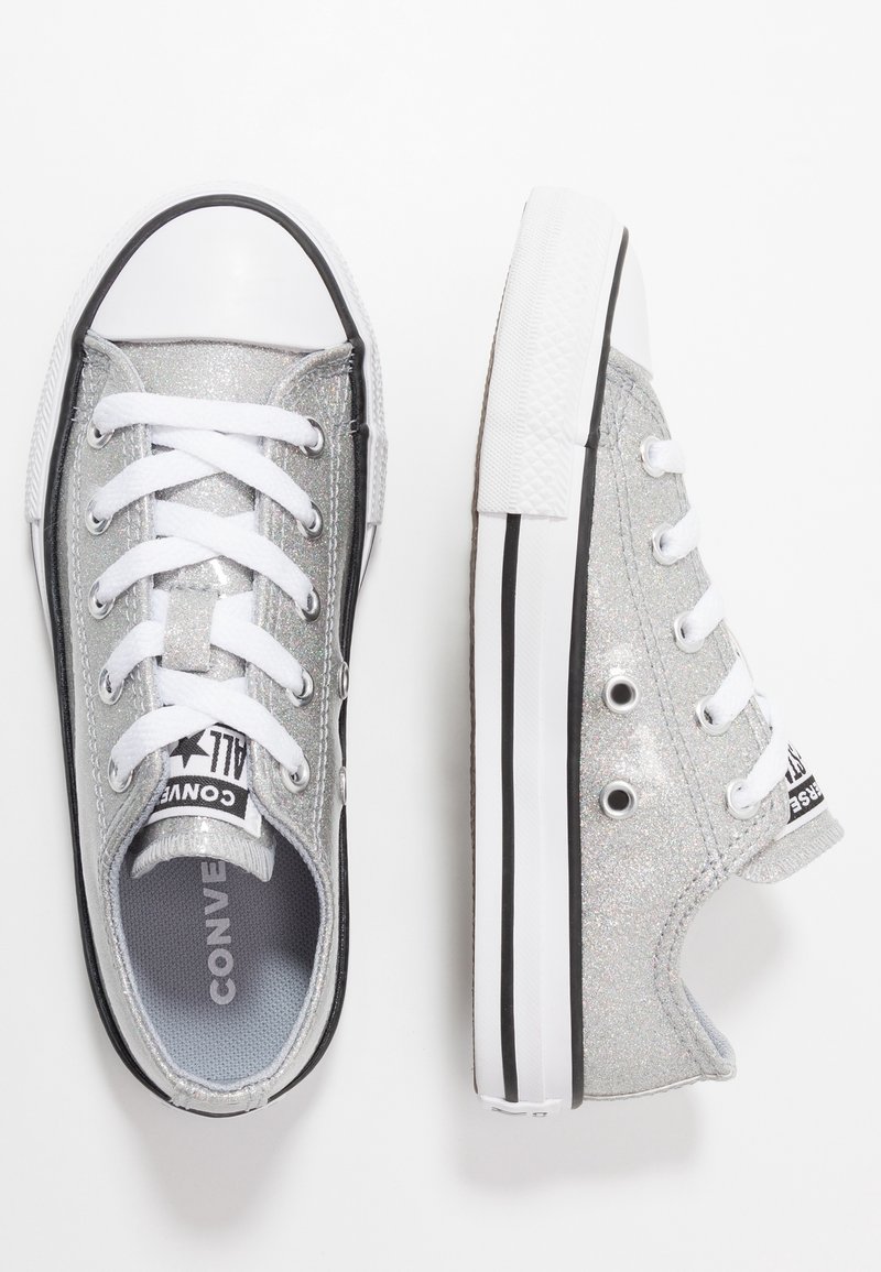 Baskets basses Converse pailletées argentées avec lacets blancs et semelles blanches à rayures noires, une chaussure vue de face, l’autre vue de côté.
