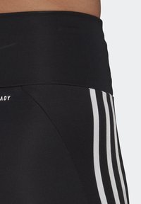 Leggings de entrenamiento negros con una cinturilla alta, que presentan detalles de rayas blancas a lo largo de los lados y una textura de tela suave y elástica.