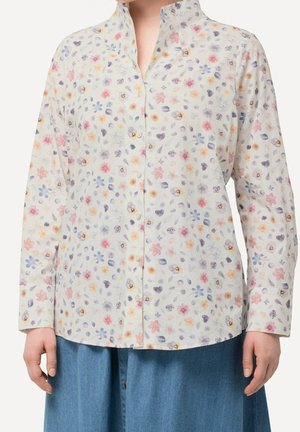 Langærmet skjorte med knapper med lille pastelfarvet blomsterprint i pink, lilla og gul, båret sammen med blå denimunderdele.