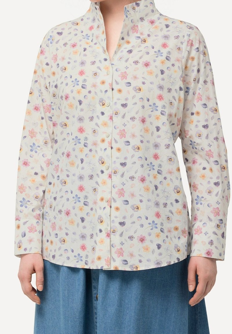 Chemise à manches longues boutonnée avec un petit imprimé floral pastel rose, violet et jaune portée avec un bas en denim bleu.