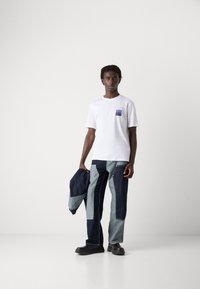White short-sleeve t-shirt with a blue pocket design, paired with multi-toned denim pants featuring varying shades of blue and a loose fit.