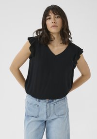 Blouse noire à col en V avec des manches volantes, texture douce, coupe décontractée, assortie à un jean en denim bleu clair. Fond uni.