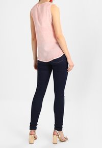 Top sans manches rose avec un ourlet arrondi, associé à un jean slim bleu foncé et des sandales à talons blocs dorées. Design simple et texture douce.