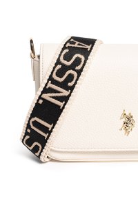 Borsa a mano bianca in pelle con una finitura testurizzata, dotata di una tracolla a motivo nero e crema, e un accento con logo oro sul davanti.