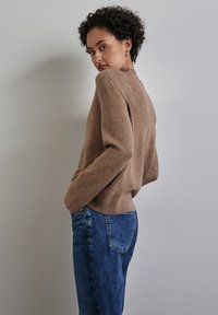 Maglione a maglia marrone con scollatura e polsini a coste, abbinato a jeans in denim blu. Il maglione ha una vestibilità comoda e una texture morbida.