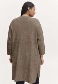 Long, loose-fitting, brown sweater made of soft, textured fabric with 3/4 sleeves and side slits at the hem.
