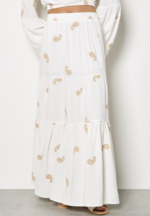 Weißer mehrlagiger Maxirock mit elastischem Bund, versehen mit hellbraunen Paisley-Mustern, getragen mit passendem weißem Oberteil und Sandalen.