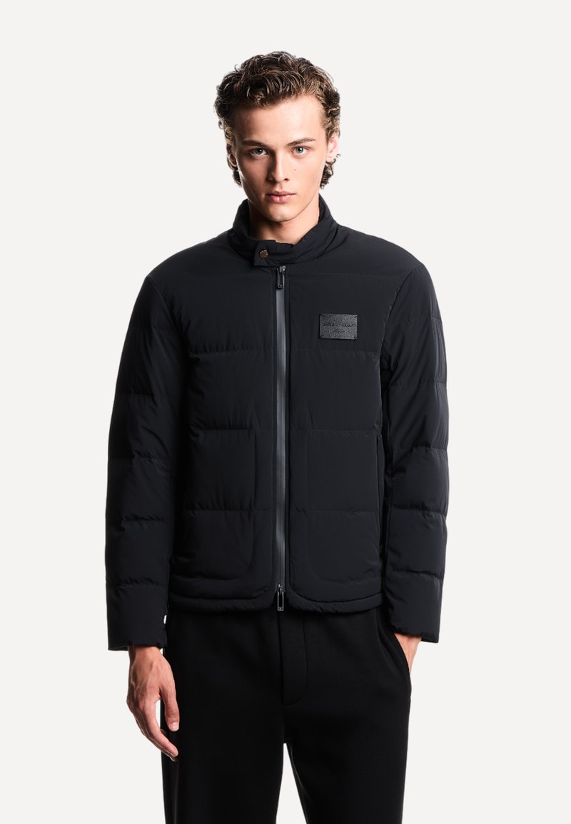 Zwarte gewatteerde jas met een hoge kraag, voorclosure met rits en twee zijzakken. Gelaagd, gewatteerd ontwerp met een logo-opdracht op de borst.
