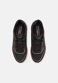 Svarta träningsskor med en strukturerad ovandel, som har diskreta perforeringar, reflexdetaljer och en dämpad sula.