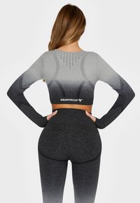 Langærmet atletisk top og højtaljede leggings i gradient grå og sort. Strukturerede mønsterdetaljer med logo ved taljen. Strækmateriale.