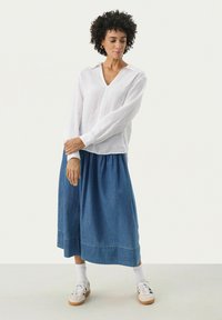 Hvid linnedbluse med lange ærmer og v-hals, parret med en denimnederdel. Nederdelen er ankel-længde med en samlet talje. Hvide sneakers.