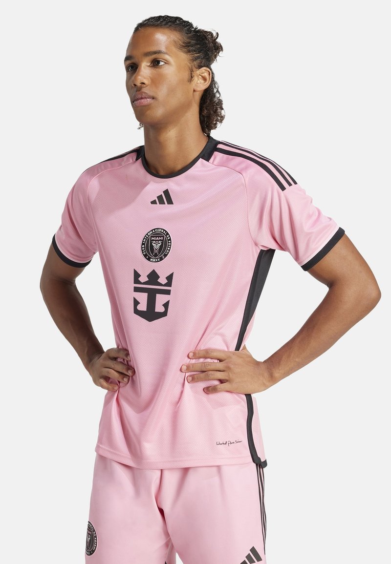 Maillot de football rose avec des accents noirs, doté d'un col rond, d'un logo au centre et de trois bandes noires sur chaque épaule.