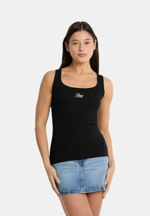 Schwarzes, geripptes Tanktop mit breiten Trägern, das ein weißes Logo in der Mitte zeigt. Kombiniert mit einem hellblauen Jeansrock.