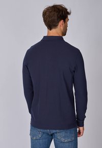 Polo shirt à manches longues de couleur marine avec un col, en tissu doux, de couleur unie et à coupe décontractée, associé à un jean en denim.