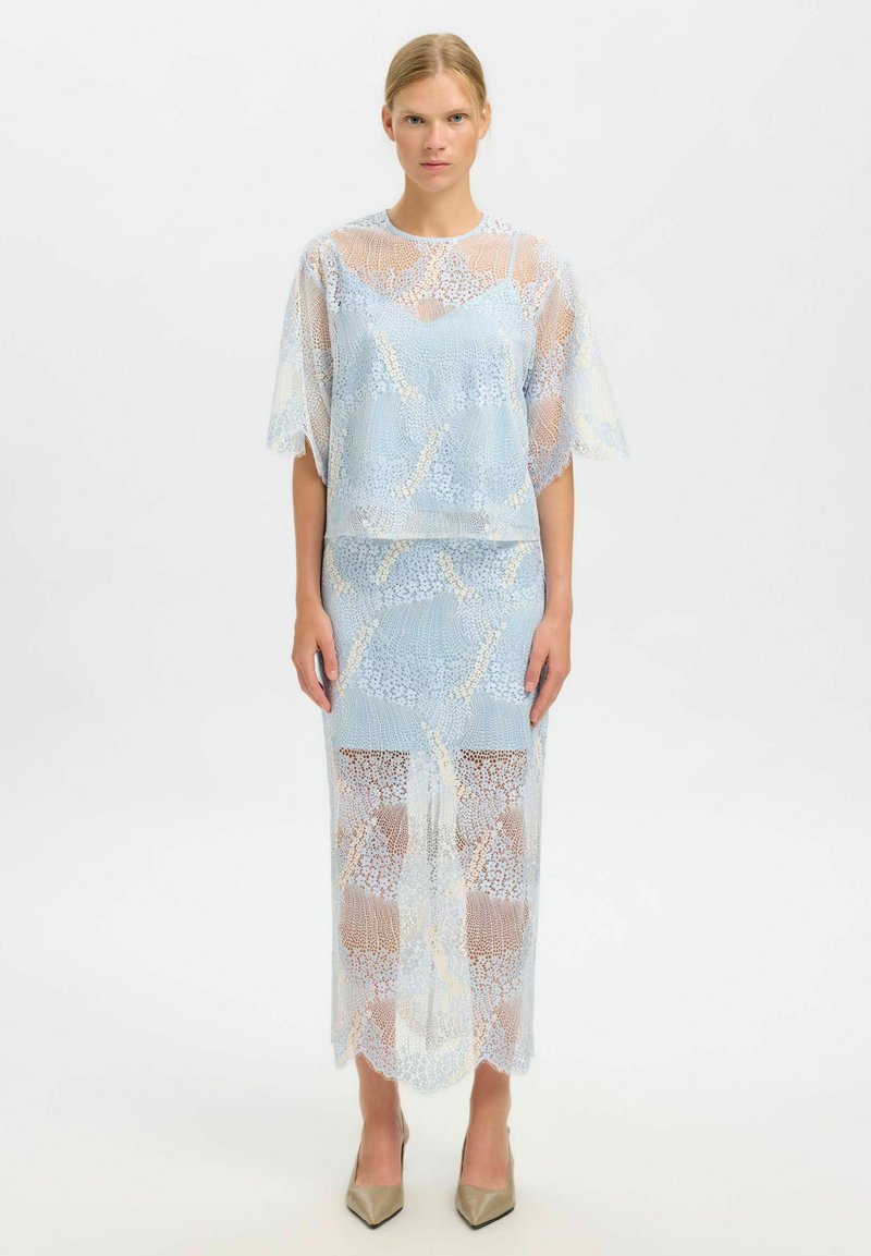 Ensemble en dentelle composé d'un haut bleu clair à manches courtes et d'une jupe assortie, tous deux ornés de motifs complexes et d'une texture transparente.