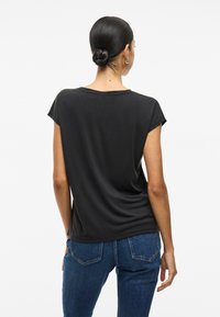 Črna kratka majica s sproščenim krojem, gladko teksturo in okroglim izrezom, v kombinaciji z visokim pasom modrih kavbojk.