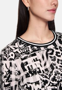 Black and white patterned sweatshirt featuring a mix of text, graphics, and leopard print. Black ribbed neckline with white accents.