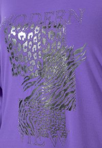 Fialová tkanina se stříbrnými a černými vzory zvířecí kůže a slovem "MODERN" ozdobeným malými kovovými nýty.