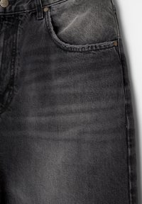 Jean en denim noir avec une finition délavée, un design à cinq poches et des coutures claires. Le tissu présente de légères variations de texture.