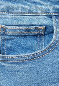 Svijetloplavi traper tkanina s stražnjim džepom koji ima vidljive šavove u kontrastnoj boji tamno smeđe. Glatka tekstura s laganim izbljeđivanjem.