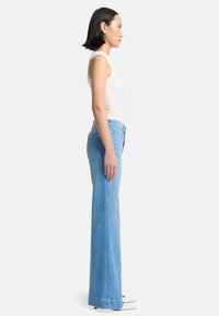 Helle blaue Jeans mit weitem Bein und hoher Taille aus Denim-Stoff. Glatte Textur, klare Linien und sichtbare Fronttaschen.