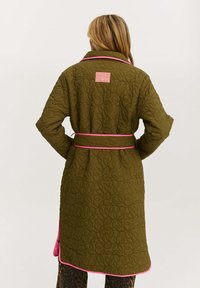 Olivovo zelený prešívaný župan s ružovými akcentmi a opaskom v páse, s textúrovaným vzorom listov a malou nášivkou na chrbte.