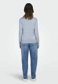 Maglione azzurro chiaro con orlo e polsini a coste, abbinato a jeans azzurri a vita alta e scarpe da ginnastica bianche.