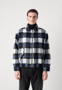 Fleece zip-up jacket with a black, white, and blue plaid pattern; features side pockets and a collar. Suitable for casual wear.
