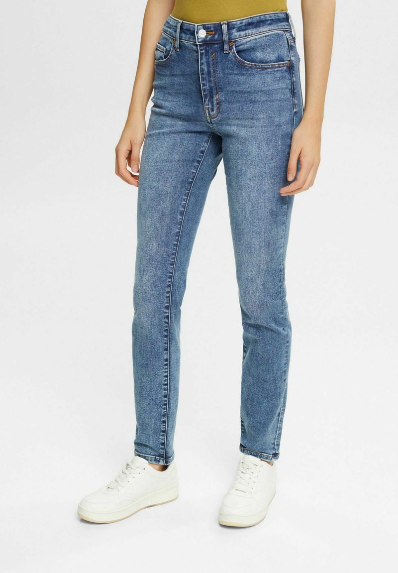 Schmale Jeans aus hellem Denim mit leichtem Verblassen, fünf Taschen und sichtbaren Nähten. Kombiniert mit weißen Sneakern.