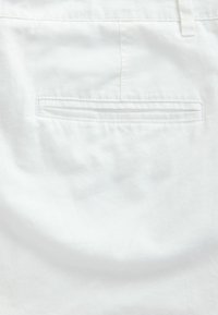 Valged linased püksid, millel on sile tekstuur, üks tagasihoidlik tasku lõhikuga ja valge niidiga õmmeldud.