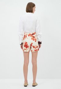 Witte lange mouwen blouse gecombineerd met high-waisted shorts met een crèmewitte basis en rode bloemenpatronen. Schoeisel is beige instappers.