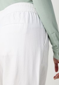 Pantalons blancs avec une finition texturée et une taille élastique, associés à un haut à manches longues de couleur verte claire avec des poignets à boutons.