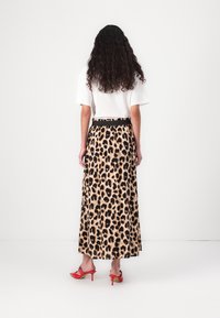 Maxikjole med leopardmønster og sort talje, parret med en hvid skjorte, vist fra ryggen, med røde stilethæle.