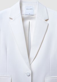 Blazer bianco realizzato in tessuto liscio, con colletto a punte, chiusura con un bottone e dettaglio centrale a piega. Etichetta con la dicitura "CALLIOPE."