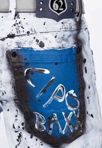 Jeans in denim con una tasca posteriore blu caratterizzata da modelli di spruzzi bianchi, dettagli neri e un emblema argento con il numero 62 in vita.